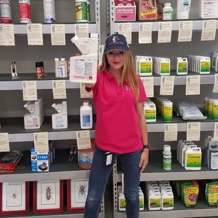 ABC Pest Control staff member in red polo holding product in front of shelves full of pest control products