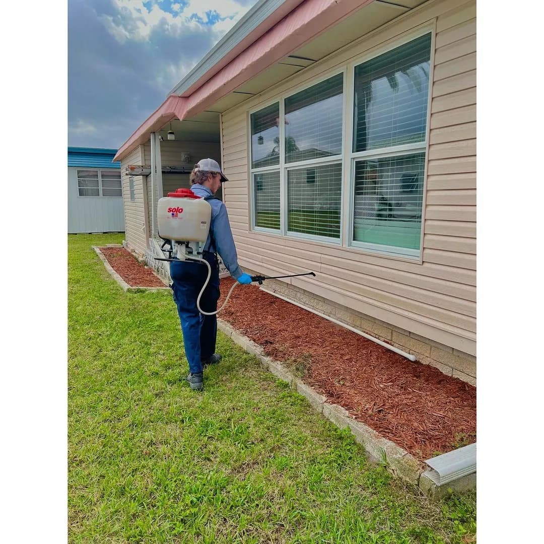 ABC Pest Control technician with backpack sprayer treating the exterior of a home